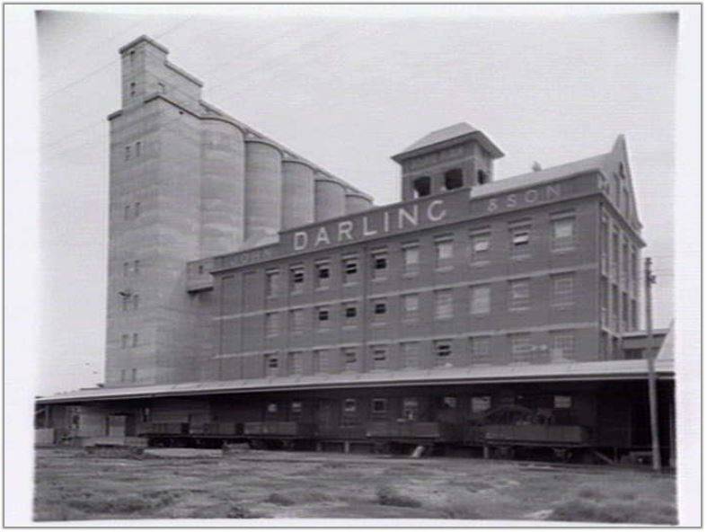 c 1940  depicting the east fa ade of the complex  including the 1926-7 mill building  rail siding  loading platform  canopy and rail cars and the 1939 concrete silos